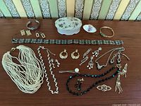 Full layout of costume jewelry lot showing necklaces, earrings, bracelets, and trinket box arranged on table.