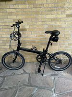 Side view of assembled black Dahon Speed P8 folding bicycle with coiled cable lock and bell on brick background