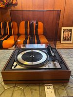 Front view of Dual 1218 record player with wood base and clear dust cover, placed on tiled floor.