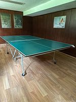 Angled view of the folded out ping pong table showing the green surface and white frame on caster wheels.