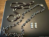 Full view of two necklaces and earrings showing amethyst beads, dark freshwater pearls and clear faceted beads alongside white freshwater pearl earrings.