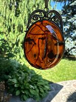 Pendant photographed outdoors against foliage background.