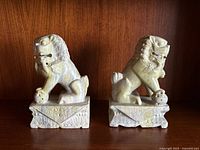 Front and side views of the two carved marble Foo Dog bookends placed on a wooden surface.