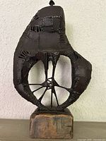 Front view of entire abstract welded metal sculpture on wooden base against wall.