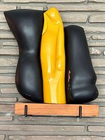 Front view of black and yellow painted wood sculpture on wood block base against stone wall