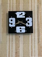 Front view of vintage Volpe clock mounted on a beige textured wall, showing black face with white bold numerals and gold-tone hands.