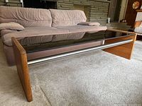 Front left angled view showing teak sides, smoked glass top, and stainless steel rods