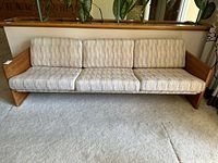 Front view of the vintage teak sling style mid-century modern sofa showing three fabric seat and back cushions and two matching pillows.