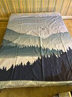 Full view of the shower curtain laid flat on a mattress, showing mountain and tree silhouettes in gradient blues.