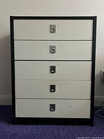 Front view of the 5-drawer dresser showing the metal handles and black frame with white drawers with some surface marks.