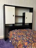 Front view of the headboard with twin bed frame and patterned blanket on mattress, showing the black and white color scheme and storage drawers on the side.