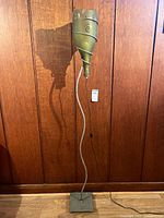 Full view of the lamp showing its tall curved steel body, square base, and wine bottle shaped lampshade with coiled metal accent.