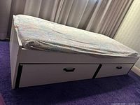 Full side view of white melamine single bed with mattress and two storage drawers.