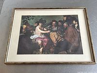 Framed print featuring Bacchus and revelers, showing the full image and frame on a gray surface.