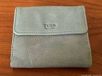 Front view of the teal leather wallet showing Tusk New York embossing on the flap and soft textured leather surface.
