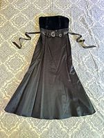 Full view of the strapless gown showing velvet top, silk skirt, and tied belt on a patterned fabric backdrop