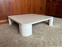 Three-quarter front view showing low-profile square table on carpet in front of wood paneling