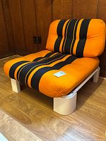 Front perspective of armchair showing orange and black striped cushions and white tubular frame
