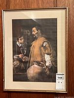 Framed print showing the full artwork and frame placed on wooden floor, the image clearly shows the man holding a clay jug with other figures in the background.