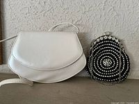 Pair of handbags side by side on shelf, showing leather bag and beaded purse.