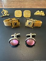 Photo showing all cufflinks and ski pins on black surface, highlighting designs and colors.