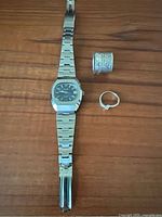 Full view of all items on wooden surface: stainless steel watch, large sterling silver ring, small silver ring.
