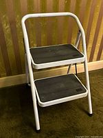 Front left angled view showing the white metal frame and two wide black rubber anti-slip steps with minor wear.