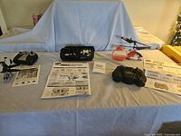 Wide view of the three Air Hogs helicopters, controllers, and instruction manuals arranged on a table with a blue cover