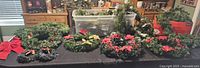 Wide view of Christmas wreaths and garlands displayed on table, showing overall inventory with decorations including red bows and poinsettias.