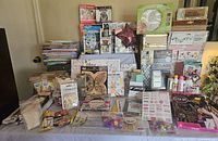 Wide view of table filled with assorted craft items including coloring books, diamond dot kits, paint bottles, stickers, and decorative boxes.
