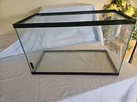 Glass fish tank sitting on a white cloth, showing front and side panel details with black frame.