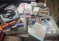 Large assortment of card making supplies including cardstock, ink pads, embossing powders, stamps, embellishments, and the embossing machine.