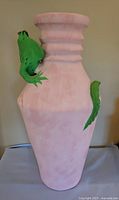 Full frontal view of the pink clay vase with green iguana attached climbing on the neck.