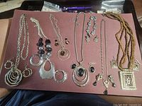Overview of various necklace and earring sets displayed on a maroon surface with a variety of pendants and bead accents