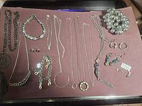 Multiple silver tone and beaded jewelry items laid out on surface including necklaces, bracelets, earrings, rings.