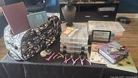 Wide shot showing all items on a black table including storage bag, organizer boxes, tools, books, display bust, magnifying glass, and bags of beads.