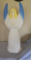 Front view of blow mold angel showing yellow hair, white robe, and blue-tipped wings.