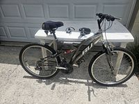 Full side view of Stinger 18-speed men's mountain bike showing frame, tires, pedals, and seat with a spare seat on the table behind