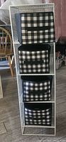 Full view of tall white metal shelving unit filled with four black and white checkered fabric baskets.