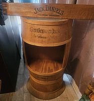 Front view of the oak barrel branded with Gentleman Jack on the middle band and Jack Daniels on the bottom band, showing open interior storage space.