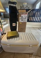 Full lot shown together: closed cooler on floor, torch kit on cooler, black canopy bag and cot box standing upright behind.