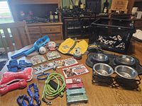 Wide photo showing the full collection of pet supplies including dog bowls, leashes, collars, life vest, toys, signs, and portable playpen.