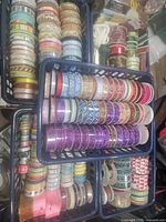 Top down view of multiple baskets containing large quantity of ribbon spools in various colors and patterns including glitter and metallic.