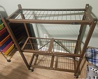 Front angled view showing the brown metal frame with wire grid shelves, wheels, and collapsible design.