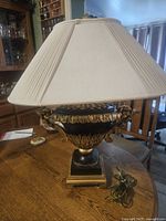 Full view of vintage urn shaped lamp on wooden table with ivory pleated shade.