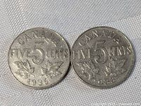 Pair of Canadian five cent coins from 1935 and 1928 showing the reverse side with 'FIVE 5 CENTS' and maple leaves.