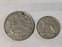 Two Swiss coins side by side; left coin is a 2 Franc coin dated 1982, right coin is 1 Franc coin featuring a dog labeled 'Reut'. Both shown on white background with visible details and condition.