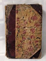 Front cover of the antique book showing marbled paper and brown leather binding with wear and cracks.