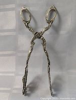 Full view of antique Italian silver plated serving tongs showing overall shape, size, and intricate decorative engravings.