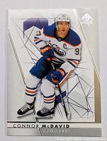 Front view of Conor McDavid hockey card in Edmonton Oilers white jersey showing hockey player with stick, including card branding and player details.